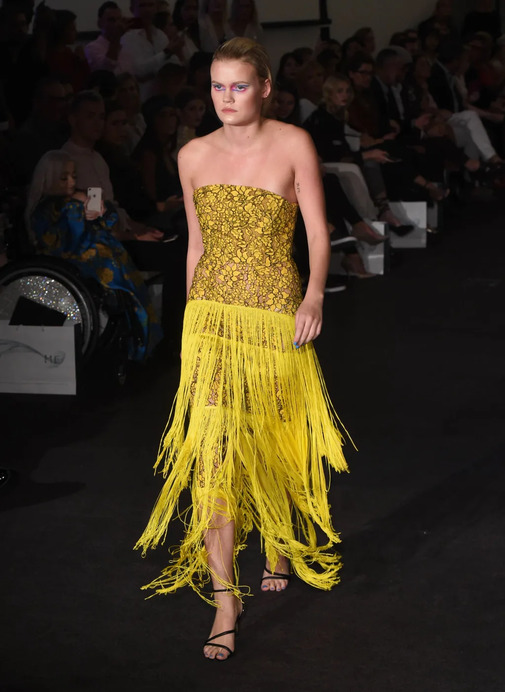 Modelă pe podium la London Fashion Week, machiaj asortat rochiei galbene cu franjuri